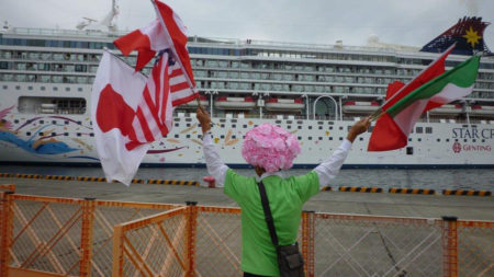両手に様々な国旗を振りながら、船に向かって中国語で呼びかけています。