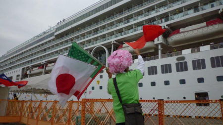 両手に様々な国旗を振りながら、船に向かって中国語で呼びかけています。